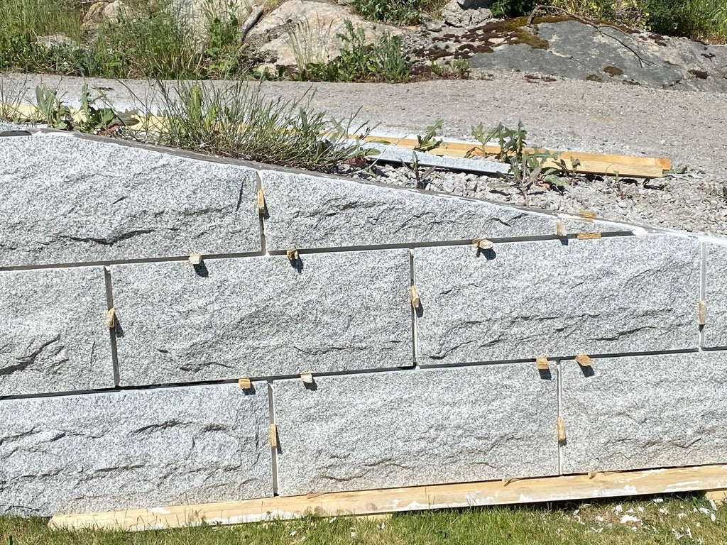 Beklädnad i granit på betongmur. Träkilar för montering. Grå. Stengrossen