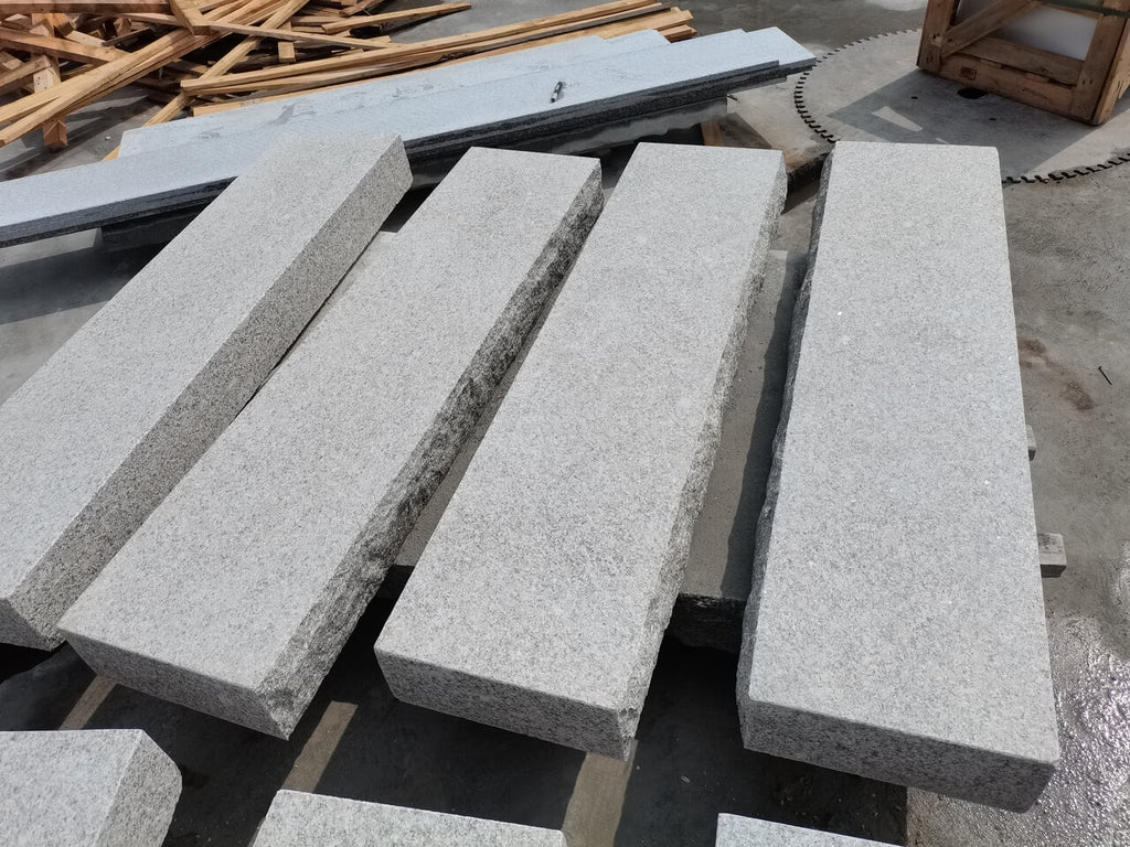 En närbild av trappsteg i granit från Stengrossen framhäver den hållbara stegytan och den råkilade framsidan, vilket ger ett robust och stilfullt utseende.