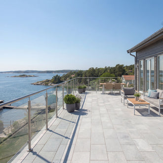 Uteplats vid havet med grå granitplattor 60x30x3 cm i solsken och möbler för avkoppling, Stengrossen säljer produkten.