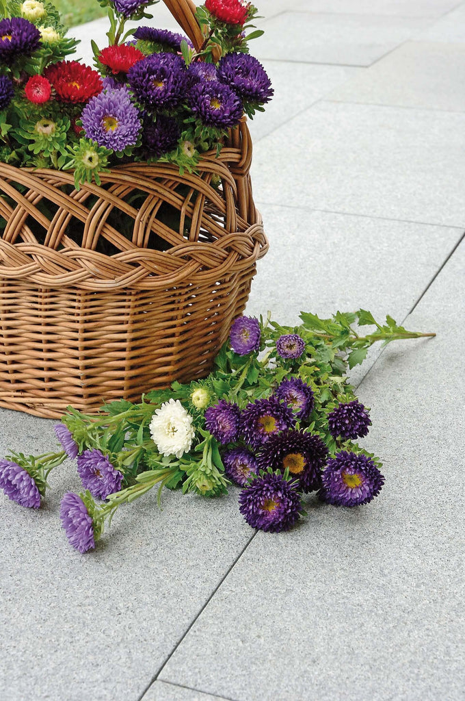 Platta av granit. Färgen är grå. Ovanpå plattorna står det en korg i rotting med blommor i Det ligger även blommor på plattorna. Säljs av Stengrossen.se