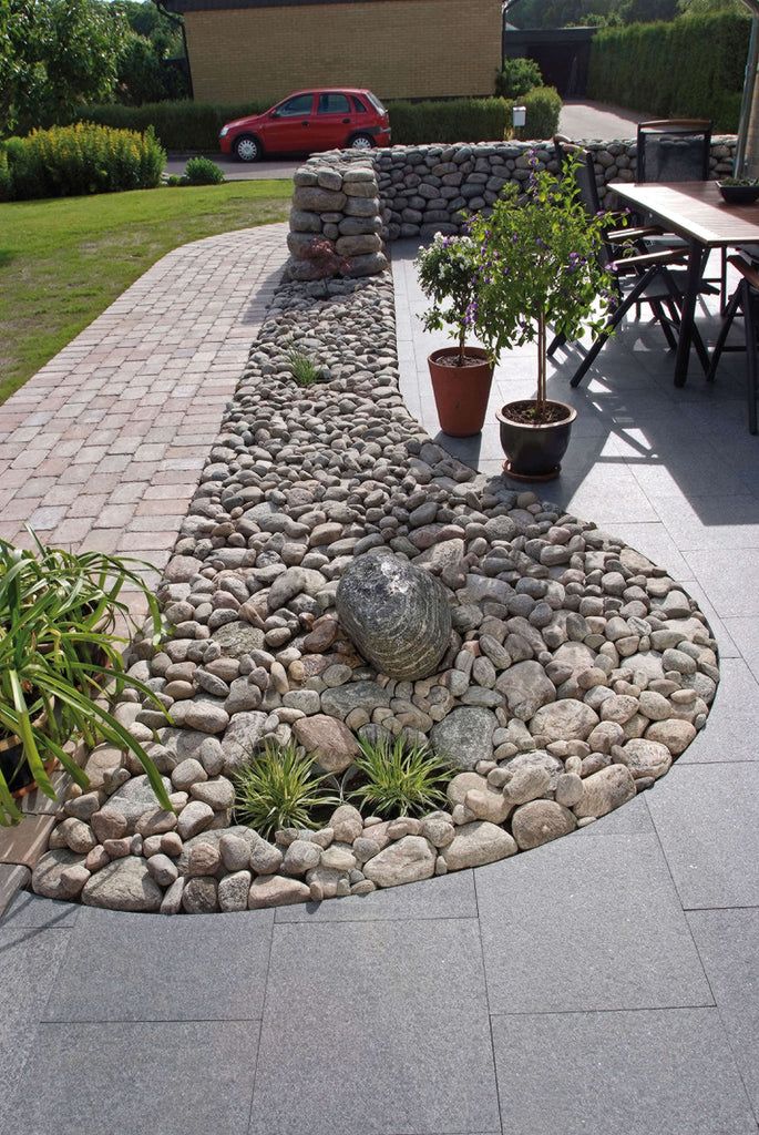 Stenplattor i granit. På insidan av plattorna ligger det kullersten. Bland kullerstenen finns det ett par gröna växter. Färgen på granitplattorna är grafit. Säljs av Stengrossen.se