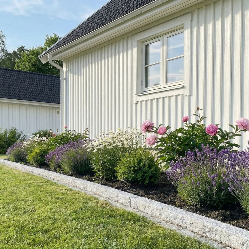 Granitkantsten som kallas för GV6 ramar in en blomsterbädd framför ett hus. På andra sidan av kantstenen är det en gräsmatta. GV6 har en storlek av 100x20x8 cm och är grå. Stengrossen säljer kantsten.
