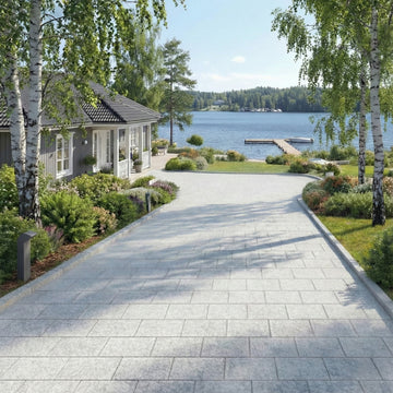 Granitplatta 30x20x6 cm använd som körbar markbeläggning vid sjönära villa med brygga och sommarblommor – Stengrossen säljer produkten.