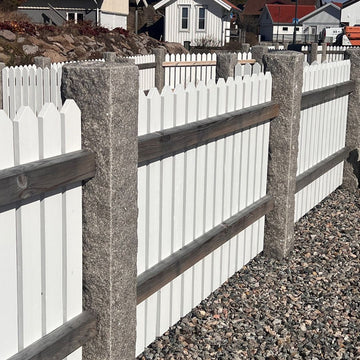 Ett antal grå granitstolpar i bohusgranit, 170x20x20 cm, med råkilad yta, totalt tio stycken. Mellan varje stolpe är ett vitt trästaket monterat. På marken nedanför stolparna ligger det dekorsten i form av makadam. Stengrossen säljer produkterna.