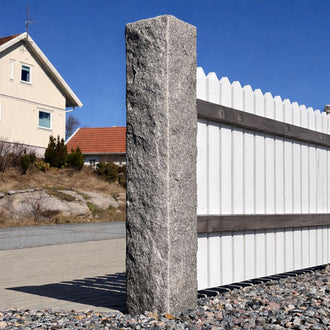 Närbild av en grå granitstolpe i färgen grå bohus, storlek 170x20x20 cm. På höger sida om stolpen är ett vitt trästaket monterat. Stengrossen säljer produkten.