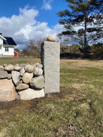 Grå granitstolpe med råhuggen yta, skapar ett naturligt och robust intryck. Stengrossen säljer produkten.