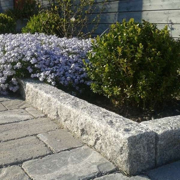 Granitkantsten i färgen Grå Bohus som ramar in en blomplantering. På utsidan ligger det grå marksten i betong. Stengrossen säljer produkterna.