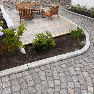 Granitkantsten GV4 i färgen grå, med måtten 100x25x10 cm, som ramar in en uteplats med träbeläggning och utemöbler. Vid denna stensättning finns även radiestenar i kantstenen, och på nedsidan av kantstenen ligger smågatsten. På ovansidan av kantstenen finns en bädd med planteringar. Stengrossen säljer produkten.