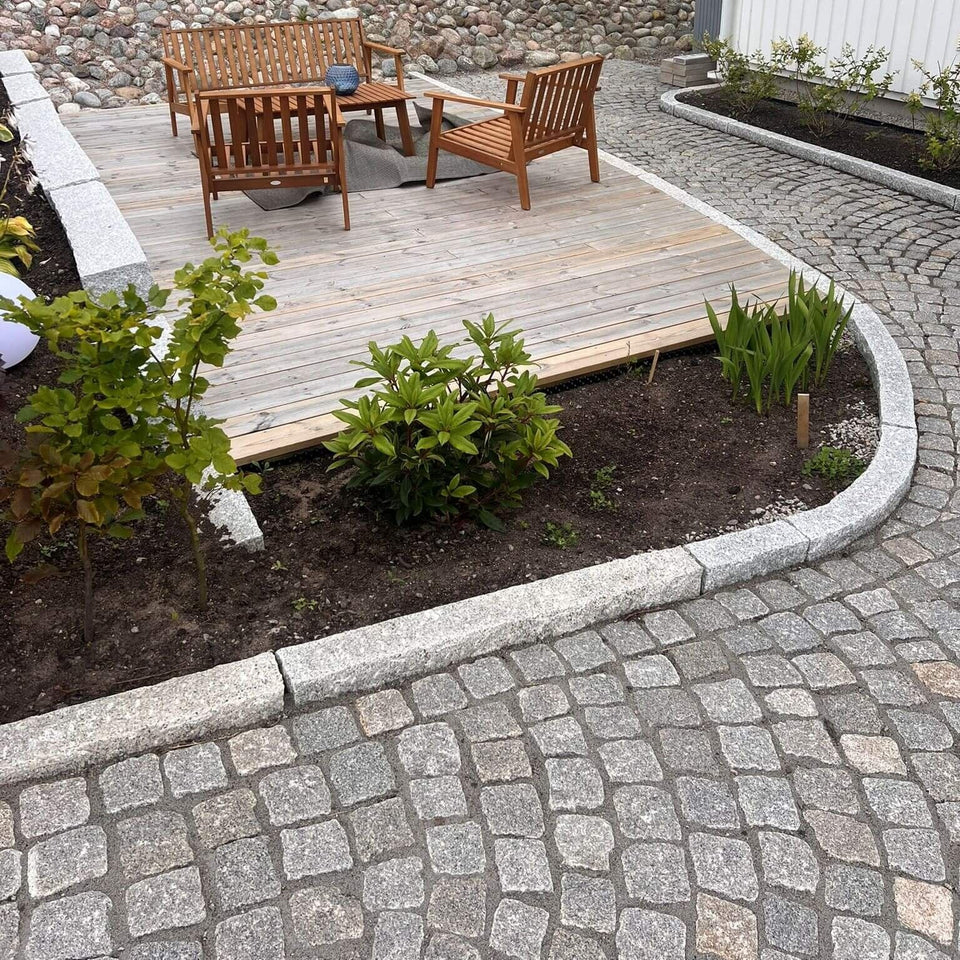 Granitkantsten GV4 i färgen grå, med måtten 100x25x10 cm, som ramar in en uteplats med träbeläggning och utemöbler. Vid denna stensättning finns även radiestenar i kantstenen, och på nedsidan av kantstenen ligger smågatsten. På ovansidan av kantstenen finns en bädd med planteringar. Stengrossen säljer produkten.