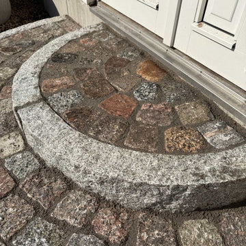 Närbild på en radiekantsten, med radie 0,5 meter, som bildar det översta steget i en trappa. Stengrossen säljer produkterna.