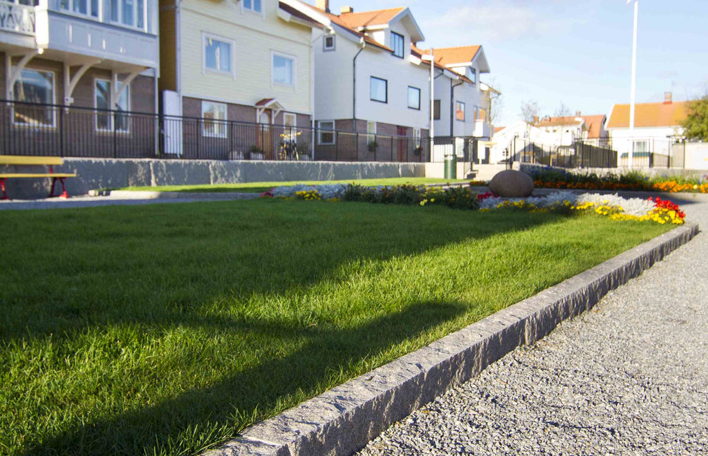 Granitkantsten RV4 i Grå Bohus, svensktillverkad och stilren. Ena sidan gränsar mot en grusbädd, medan den andra övergår i en grönskande gräsmatta. Stengrossen säljer produkten.