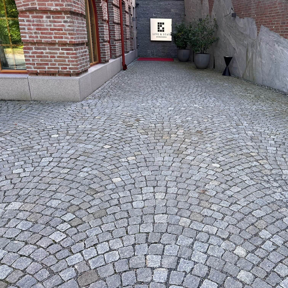 Smågatsten av sorten Grå Bohus lagd längs exklusivt hus med sågad bergvägg på höger sida – Stengrossen säljer produkten.