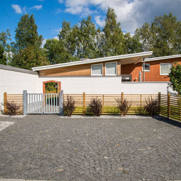 Garageuppfart med svart gatsten, typ Bodafors. Gatstenen är lagd i bågmönster. I bakgrunden finns det ett hus med tillhörande trädgård. Säljs av Stengrossen.se