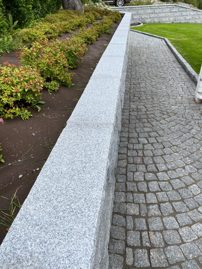 Smågatsten från Portugal. Inramad av kantsten i granit samt en mur i granit. På toppen av muren ligger det en Avtäckning i granit. Säljs av Stengrossen.se