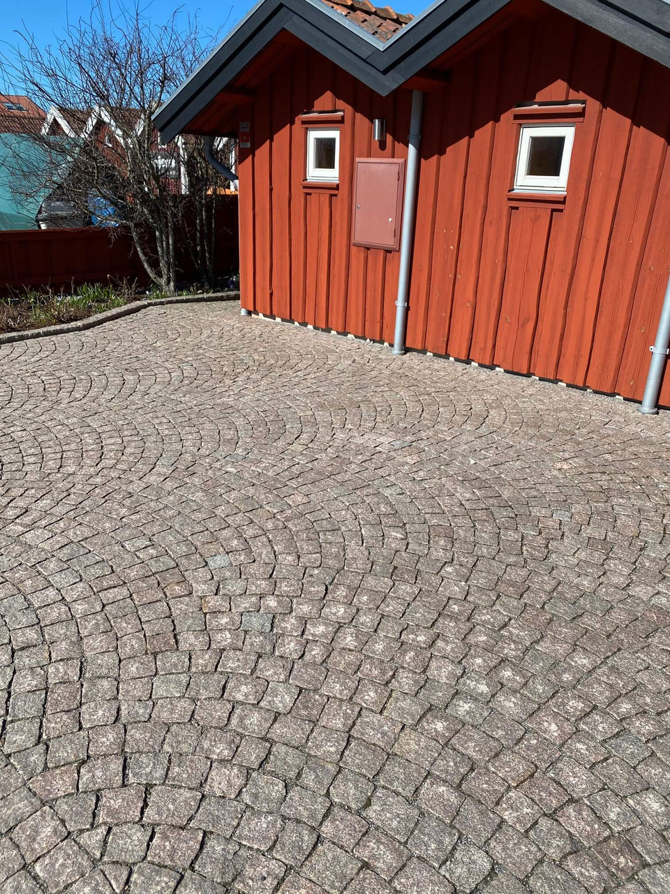 Röd gatsten från Bohuslän. Gatstenen kallas också för knott eller smågatsten. Bågsättning. I bakgrunden finns det en röd sjöbod. Säljs av Stengrossen
