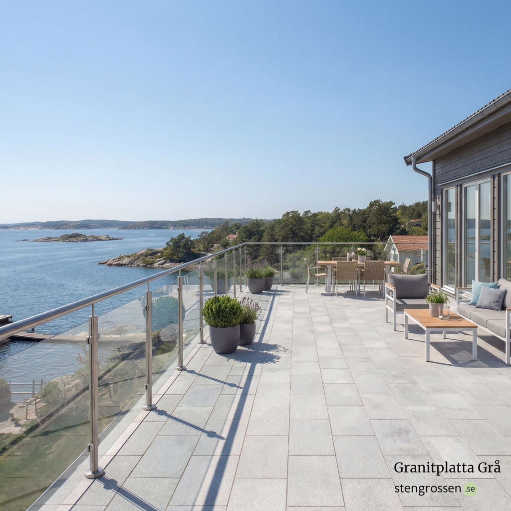 Solbelyst altan med grå granitplatta 60x30x3 cm, moderna möbler och blomsterarrangemang intill glasräcke vid skärgårdsmiljö; Stengrossen säljer produkten.