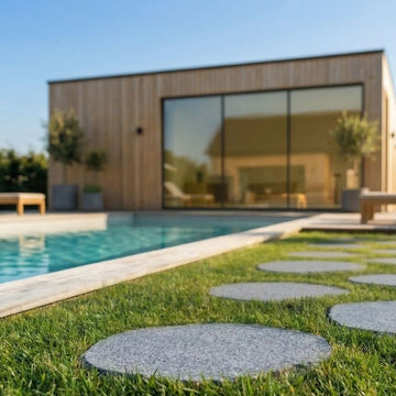 Trampstenar som är graftfärgade ligger i en gräsmatta som går runt en pool. Stengrossen säljer trampstenar.