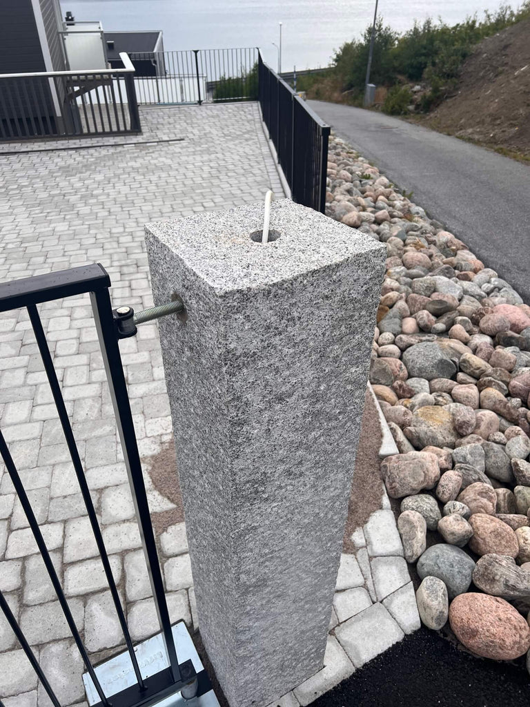 Inzoomad bild på en granitstolpe 170x30x30 cm med borrat genomgående hål, där en elkabel kommer ut för montering av lampa ovanpå, Stengrossen säljer produkten