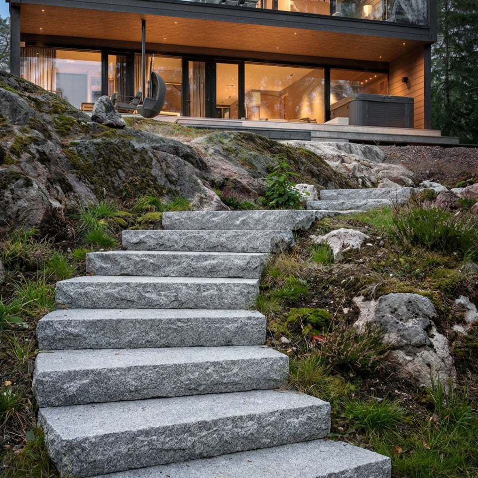 Trappsteg av grå granit som Stengrossen säljer, monterade i en slänt nedanför funkishus.