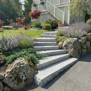 Stengrossens grå granittrappsteg i en svängd utomhustrappa vid ljusgrönt hus.