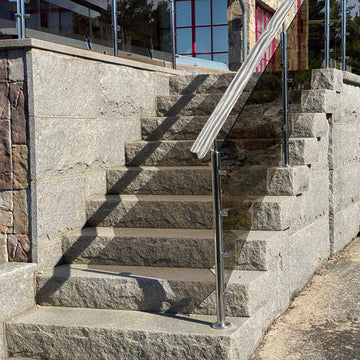 Trappa med trappsteg i Grå Bohus som leder upp mot ett poolområde. Glasräcke sitter på trappans högra sida. Produkterna säljs av Stengrossen.