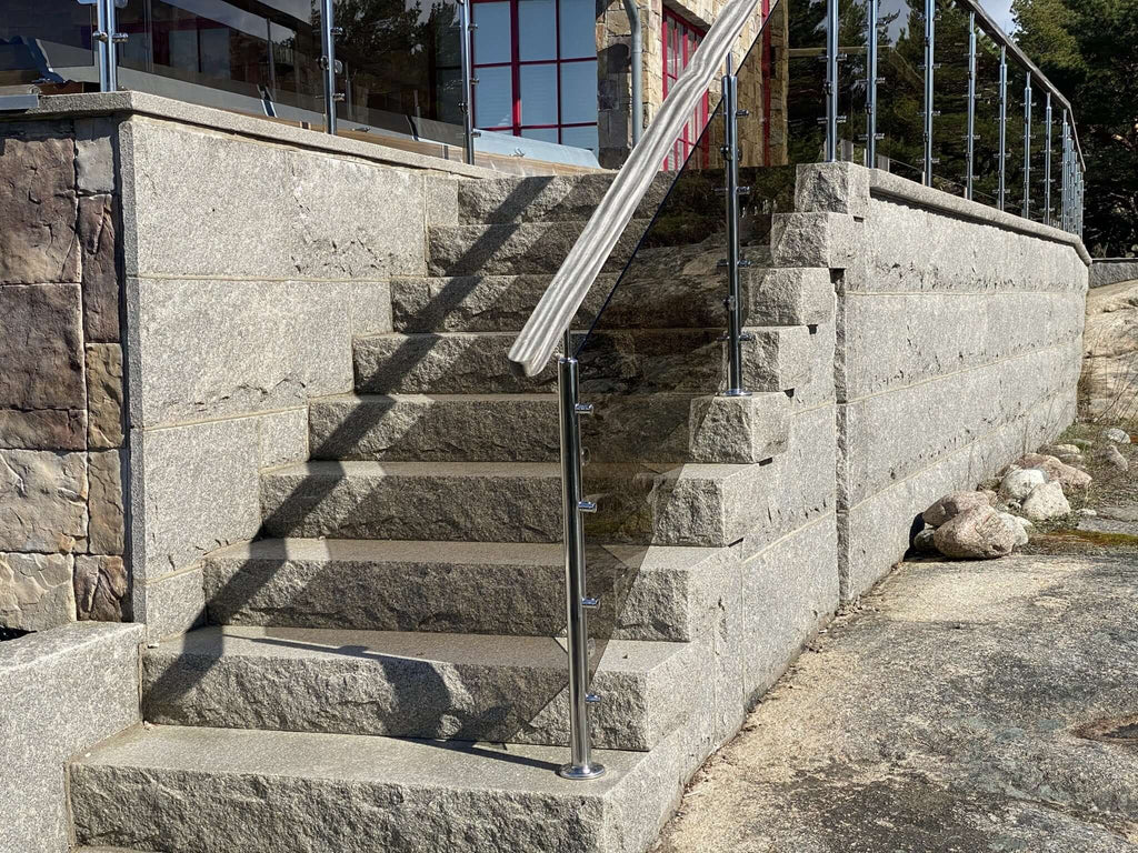 Bild på trappa i granit med ca 10 steg, monterat glasräcke i rostfritt stål och beklädnadsgranit som klär trappans sidor. Stengrossen säljer produkten.