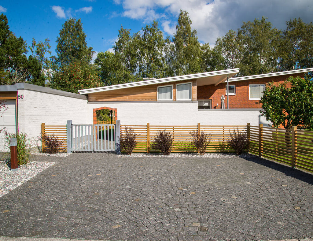 Garageuppfart med svart gatsten, typ Bodafors. Gatstenen är lagd i bågmönster. I bakgrunden finns det ett hus med tillhörande trädgård. Säljs av Stengrossen.se