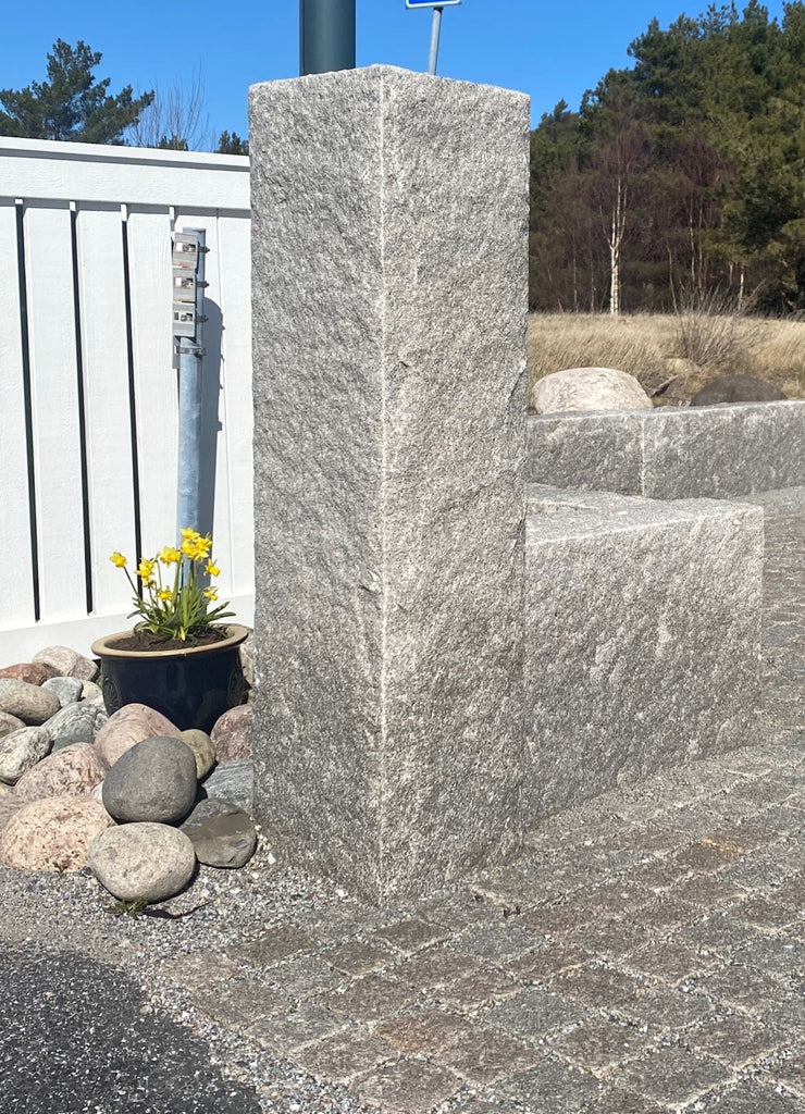 Grå granitstolpe med råhuggen yta, skapar ett naturligt och robust intryck. Stengrossen säljer produkten.