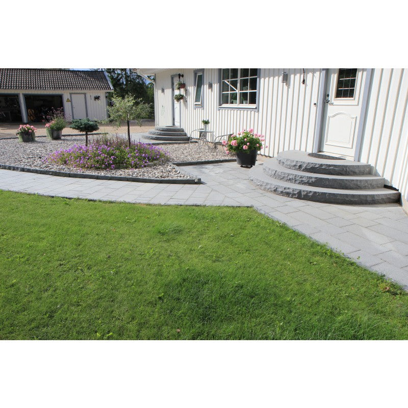 Ett vitt hus med trappa, plattor och kantsten i granit. All granit är grafitfärgade. På hitsidan av kantstenen är det en gräsmatta och på bortsidan är det dekorsten av svartvit sjösten. Säljs av Stengrossen.se