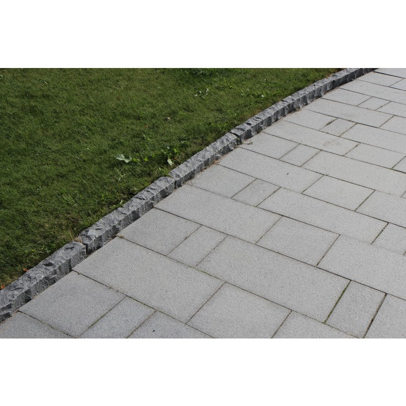 Granitplatta. Färgen är grafit. Olika storlekar. På utsidan av kantstenen är det en gräsmatta. Säljs av Stengrossen.se