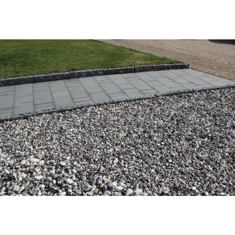 Svartvit sjösten (dekorsten) ligger framför en gång med granitplattor. Gången med granitplattor ramas in med kantsten av granit. Graniten har färgen grafitgrå. All produkter säljs av Stengrossen.se