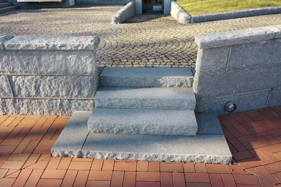 Blocksteg i Grå Bohus, en granit från Bohuslän, med flammad ovansida och råkilade kanter för en stilren och stabil trappa. Stengrossen säljer produkten.
