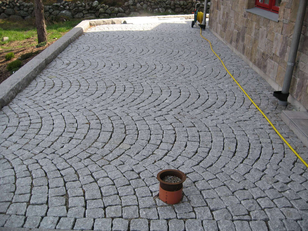 Gatsten, smågatsten, från Portugal. Lagt i bågmönster. Till vänster finns det en stenmur. Till höger är det ett hus. Gatstenen lagt i bågmönster. Säljs av Stengrossen.se