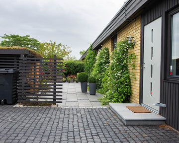 En entré till ett hus med gatsten av typen Bodafors. Gatstenen är lagd i rakmönster. I bakgrunden är det stenplattor. Framför huset, som r till höger, ligger det också plattor i granit. Säljs av Stengrossen.se