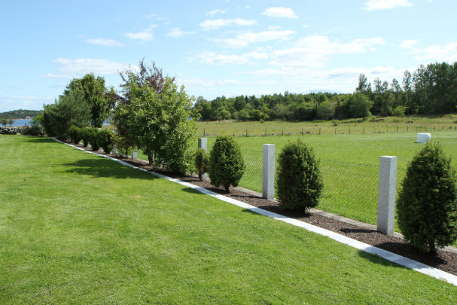 Flammade granitstolpar i harmonisk placering i en grönskande trädgård. Stengrossen säljer produkten.