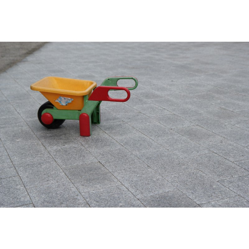 Körbar platta i granit. Storleken är 30x20x6 cm. Färgen är grå. Liten skottkärra i färgerna gul, grö och röd står ovanpå plattorna. Säljs av Stengrossen.se