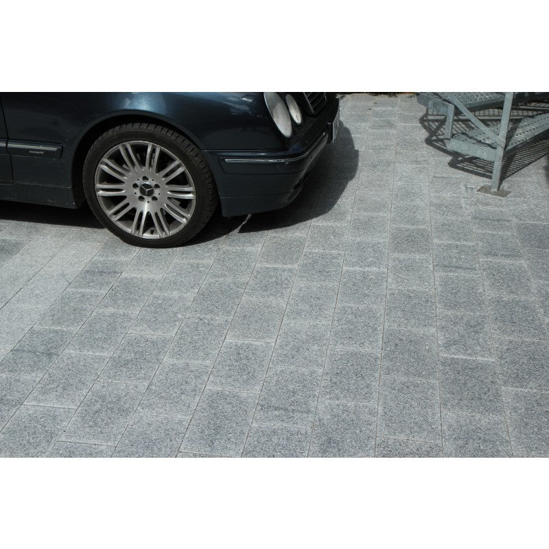 Grå granitplatta som går att köra bil på. Storleken är 30x20x6 cm. I övre delen av bilden står en bil parkerad och man ser en trappa också. Säljs av Stengrossen.se